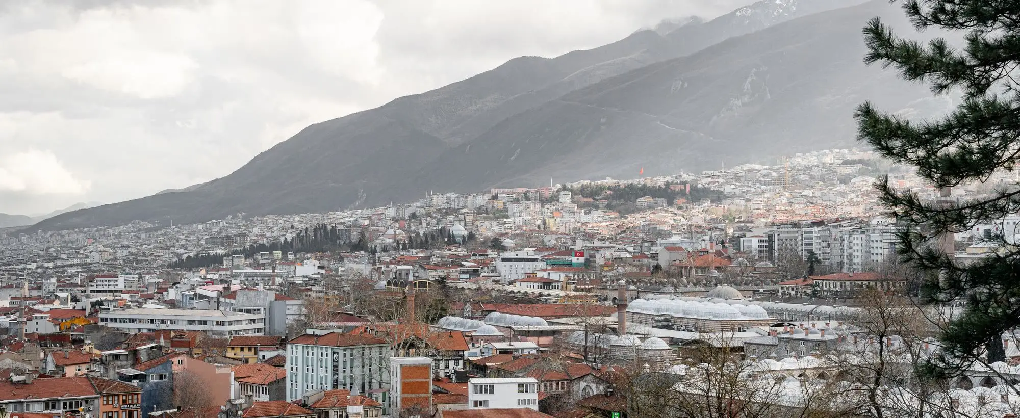Uludağ'ın eteğine yayılan Bursa; önde kiremit çatılar ve çarşının kubbeleri
